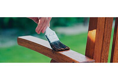 kobieta rozprowadzająca pędzlem impregnat na drewnianych meblach w ogrodzie