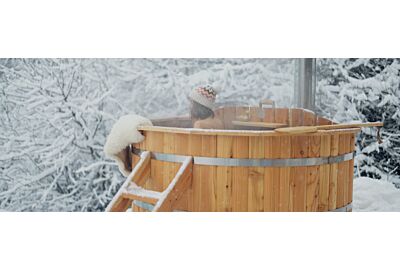 kobieta ubrana w zimową czapkę korzystająca z kapieli w balii ogrodowej w okresie zimowym