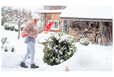 Kobieta w beżowym płaszczu i czapce doglądająca ogrodu zimową porą