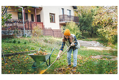 kobieta ubrana w kamizelkę i jesienne spodnie grabiąca liście w ogrodzie 