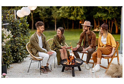 Kobieta z psem spędzająca czas w ogrodzie przy palenisku ogrodowym ze szklarnią w tle, obok wygodny biały fotel z technorattanu