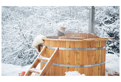 kobieta ubrana w zimową czapkę korzystająca z kapieli w balii ogrodowej w okresie zimowym