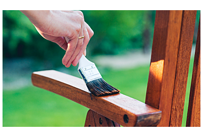 kobieta rozprowadzająca pędzlem impregnat na drewnianych meblach w ogrodzie