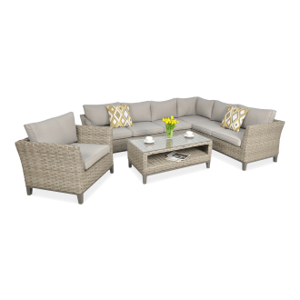 Zestaw ogrodowy z technorattanu w kolorze beżowym z narożnikiem, fotelem i stolikiem kawowym ze szklanym blatem, dekorowany żółtymi poduszkami i wazonem z tulipanami.