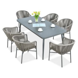 Zestaw nowoczesnych mebli ogrodowych z prostokątnym stołem w grafitowym kolorze i sześcioma fotelami z plecionym oparciem, dekorowany wazonem z żółtymi tulipanami i filiżankami.
