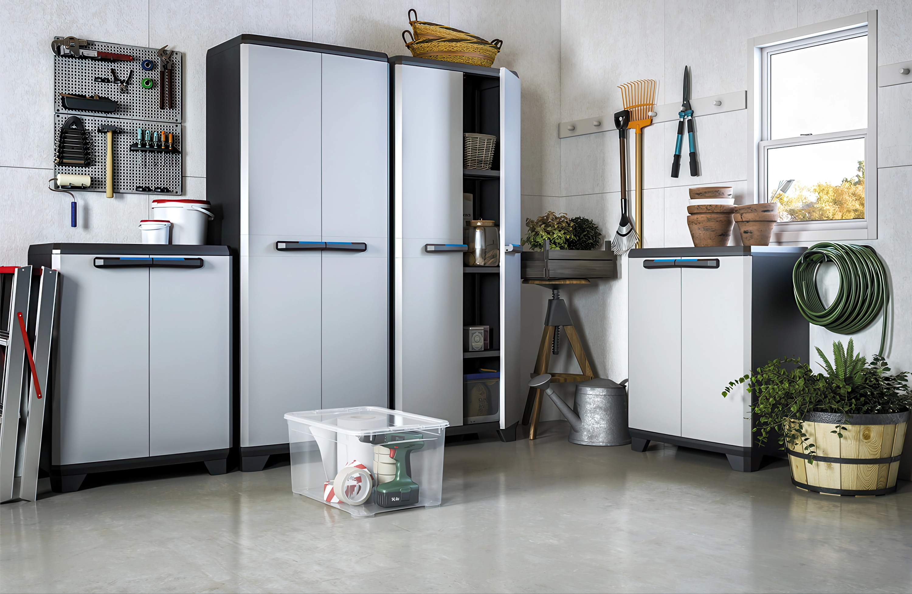 Zestaw szaf ogrodowych w jasnoszarej kolorystyce ustawionych w warsztacie, na ścianie narzędzia i akcesoria ogrodnicze.