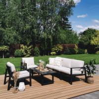 Zestaw mebli ogrodowych na tarasie z drewnianych desek, w tle ogród z wysokimi drzewami i krzewami.