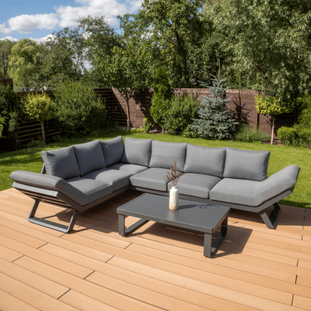 Nowoczesny narożnik TROFEO Dark Grey w ogrodzie na drewnianym tarasie. Wytrzymała, aluminiowa konstrukcja i grube, wygodne poduszki z olefinu sprawiają, że zestaw jest idealny do relaksu na świeżym powietrzu.
