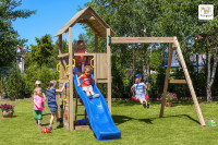 Zdjęcie przedstawia dzieci bawiące się na drewnianym placu zabaw z wieżyczką, niebieską zjeżdżalnią i huśtawką, usytuowanym na zielonym trawniku w ogrodzie. W tle widoczne są drzewa, krzewy i fragment budynku.