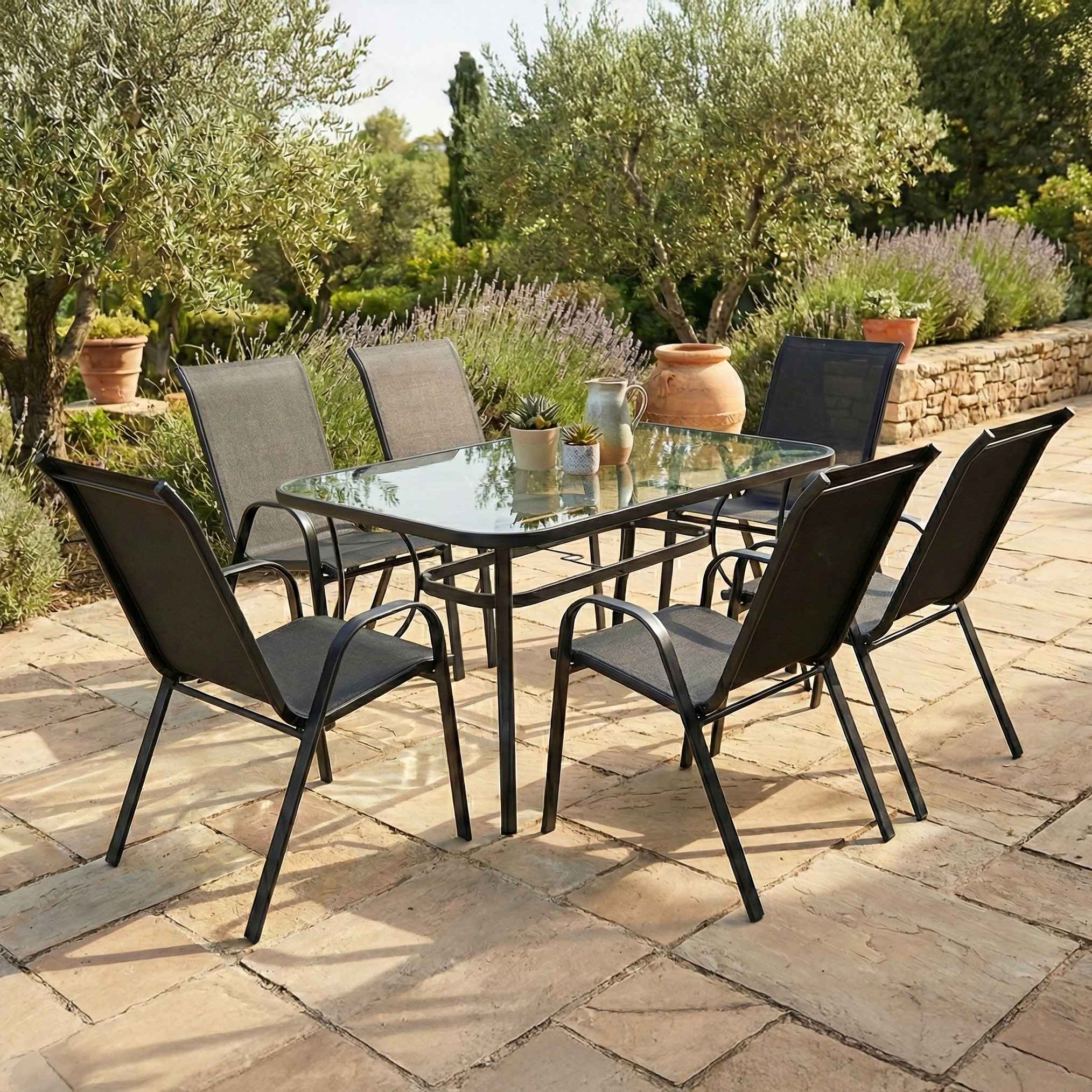 Zestaw ogrodowy BOLOGNA 150/6 Black BJORKKA prezentowany na kamiennym tarasie wśród lawendy, krzewów ozdobnych i drzewek oliwnych.