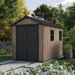 Domek na narzędzia DECO APEX 759/975 ASHWOOD - Keter w otoczeniu ogrodu z alejką i kwitnącymi krzewami