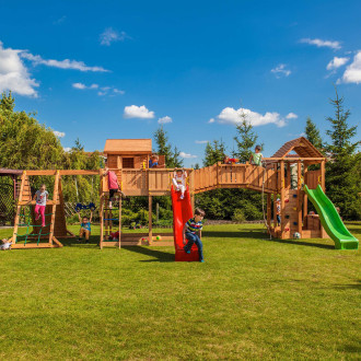Duży drewniany plac zabaw dla dzieci w ogrodzie z mostkiem zjeżdżalniami i huśtawkami aranżacja