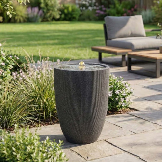 Fontanna ogrodowa grafitowa ustawiona na tarasie w otoczeniu roślin i mebli ogrodowych