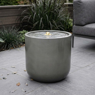 Fontanna ogrodowa w kształcie cylindra ustawiona na tarasie obok mebli ogrodowych aranżacja