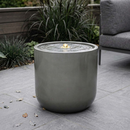 Fontanna ogrodowa w kształcie cylindra ustawiona na tarasie obok mebli ogrodowych aranżacja