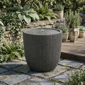 Fontanna ogrodowa w kształcie cylindra ustawiona na kamiennej nawierzchni w ogrodzie aranżacja