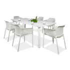 Stół jadalniany i sześć krzeseł w kolorze białym na jednolitym, jasnoszarym tle. Blat rozkładanego stołu ma perforowane wzory, a krzesła mają ażurowe oparcia i siedziska, przypominające plecionkę. Na blacie stołu stoi mała, zielona roślina w doniczce i bi