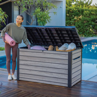 Kobieta chowająca różową matę do ćwiczeń do otwartej skrzyni ogrodowej przy basenie.