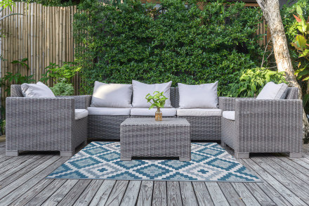 Niebiesko biały dywan z geometrycznym wzorem na tarasie przy zestawie mebli ogrodowych