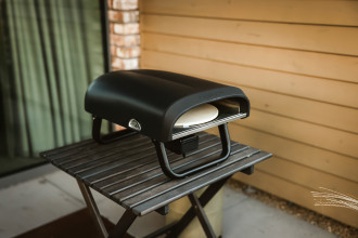 Piec gazowy do pizzy położony na małym, drewnianym stoliku