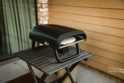 Piec gazowy do pizzy położony na małym, drewnianym stoliku