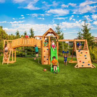 Duży drewniany plac zabaw w ogrodzie z mostkiem zjeżdżalnią huśtawką i ścianką wspinaczkową