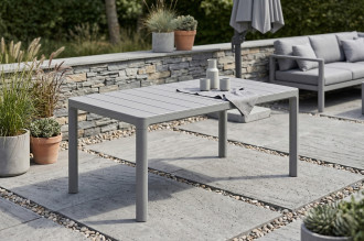 St&oacute;ł ogrodowy SCANDI DINING Storm grey Keter ustawiony na tarasie z kamiennym murem w tle
