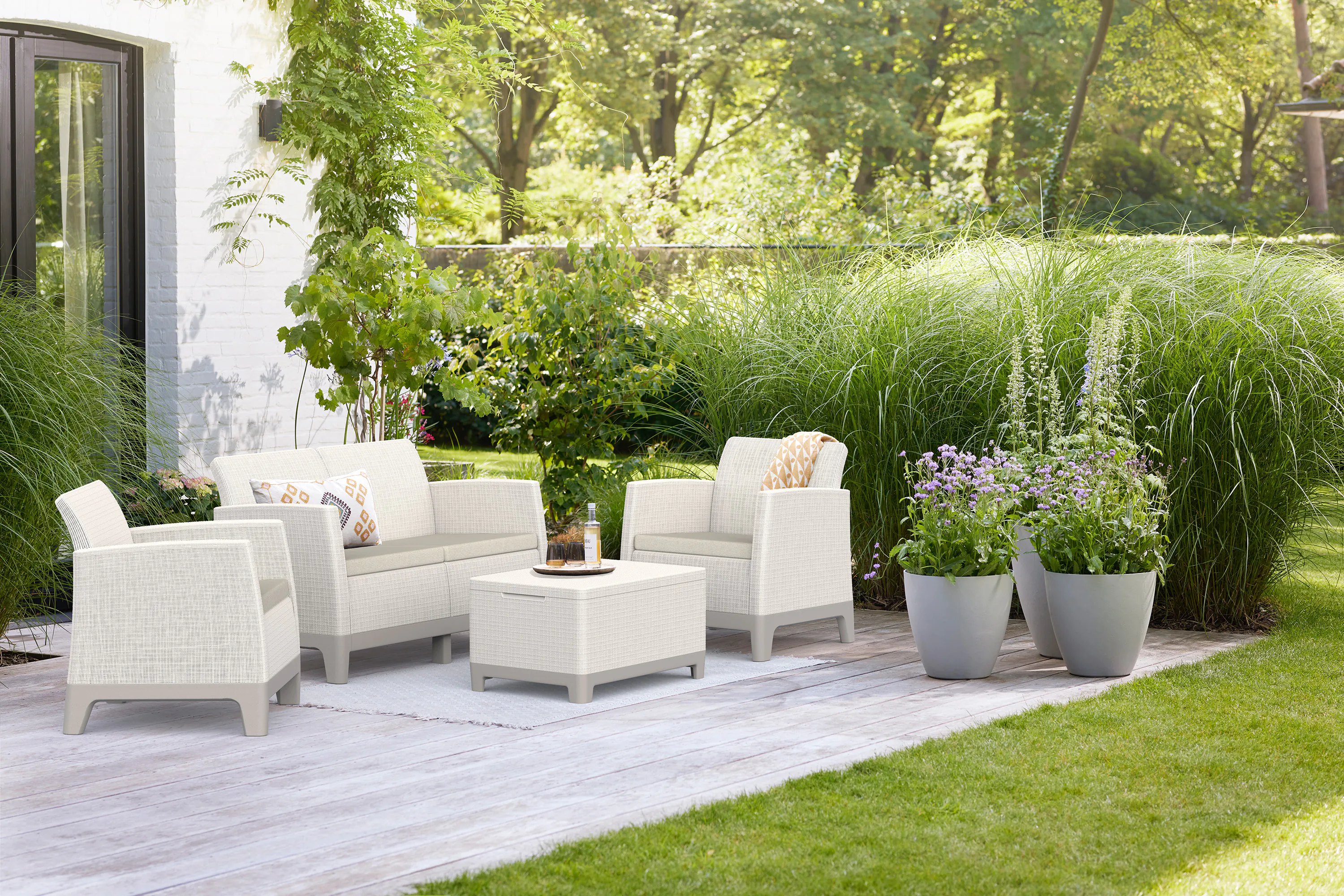 Zestaw mebli tarasowych Keter Scandi Forma Pebble Grey-Soft Beige/oat na drewnianym tarasie z roślinnością w tle
