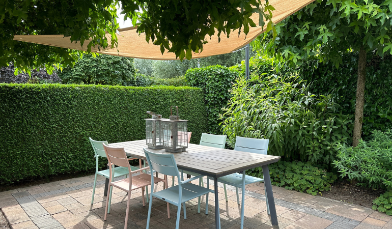 żagiel cieniujący w ogrodzie na stołem i krzesałami ogrodowymi 