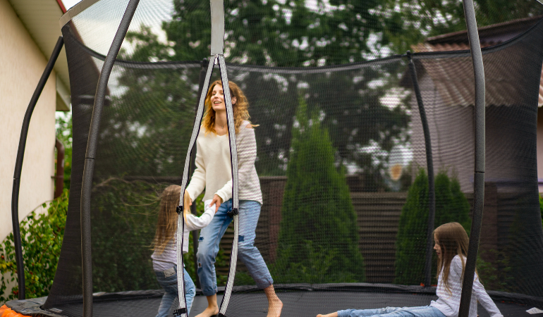 kobieta bawiąca się z c&oacute;rkami na trampolinie 