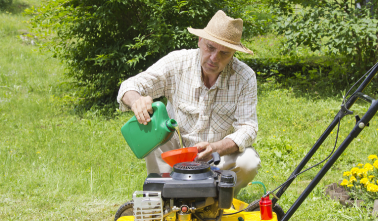 ogrodnik w słomkowym kapeluszu wymieniający olej w kosiarce 