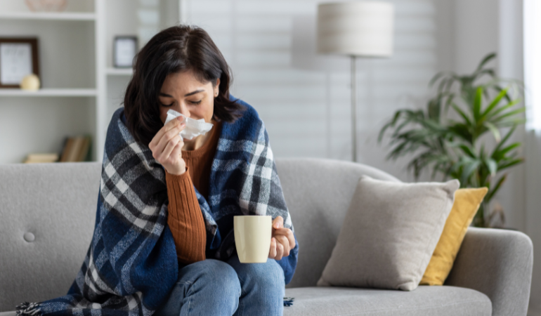 przeziębiona kobieta siedzi owinięta kocem na kanapie i wyciera nos chusteczka higieniczną 
