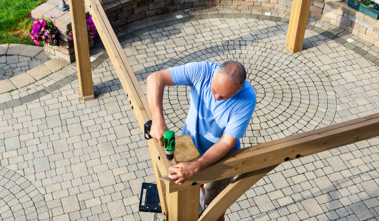 mężczyzna montujący drewnianą pergolę ogrodową 