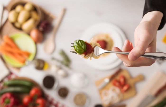 kucharz trzymający widelec ze spaghetti i listkiem bazylii na g&oacute;rze