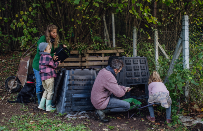 Rodzina usuwa kompost z kompostownika w ogrodzie i kompostuje odpady kuchenne w kompostowniku. Ko