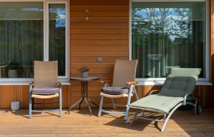 Zdjęcie z bliska części domu z otwartym tarasem, drewnianym krzesłem i stołem na zewnątrz oraz dużymi oknami