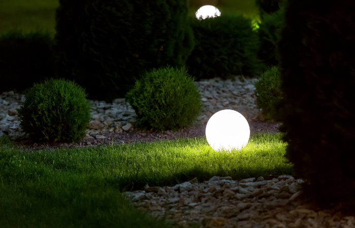 lampa ogrodowa w kształcie kuli ustawioan na trawie obok zielonego klombu
