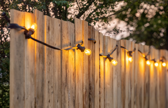 Przytulne żar&oacute;wki ustawione w rzędzie przy drewnianym płocie ogrodowym.