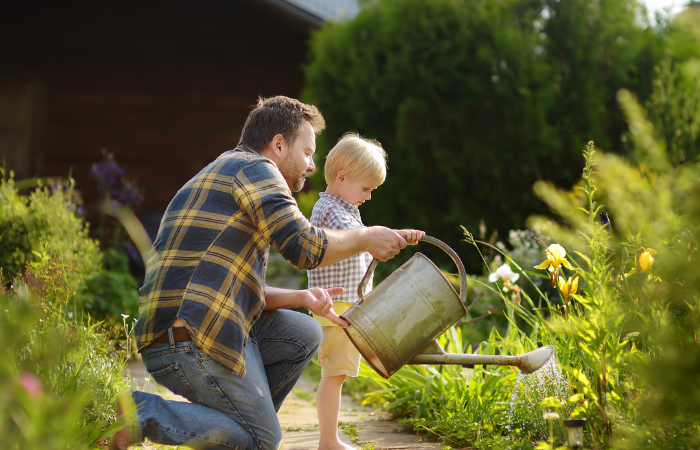 Mężczyzna w średnim wieku i jego mały syn podlewania kwiat&oacute;w w ogrodzie w letni słoneczny dzień. ogrodnictwo z małym dzieckiem i rodziną