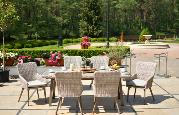 krzesła z beżowego technorattanu ustawione w ok&oacute;ł dużego stołu w ogrodzie 