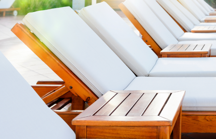 drewniane leżaki z białymi poduszkami i stolikami ustawione w rzędzie na tarasie 