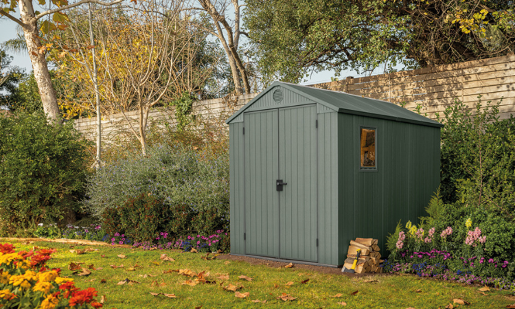 zielony domek na narzędzia ustawiony w ogrodzie pod murem