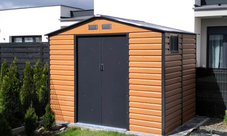 brązowy domek na narzędzia z dwuspadowym dachem ustawiony w ogrodzie obok domu
