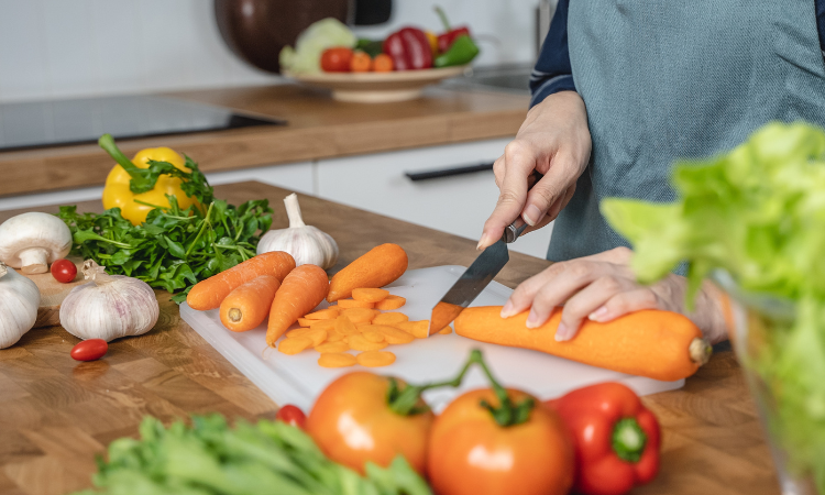  gospodyni domowa kroi marchewkę, aby przygotować składniki sałatki na obiad w kuchni