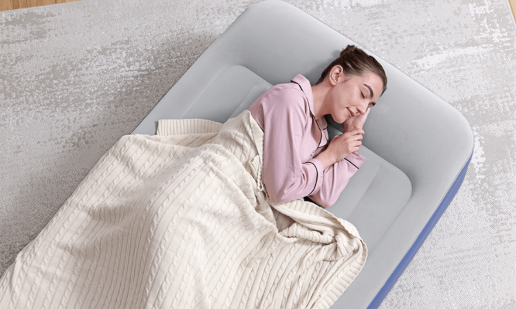 kobieta śpi w r&oacute;żowej piżamie na materacu dmuchanym pod beżowym kocem 