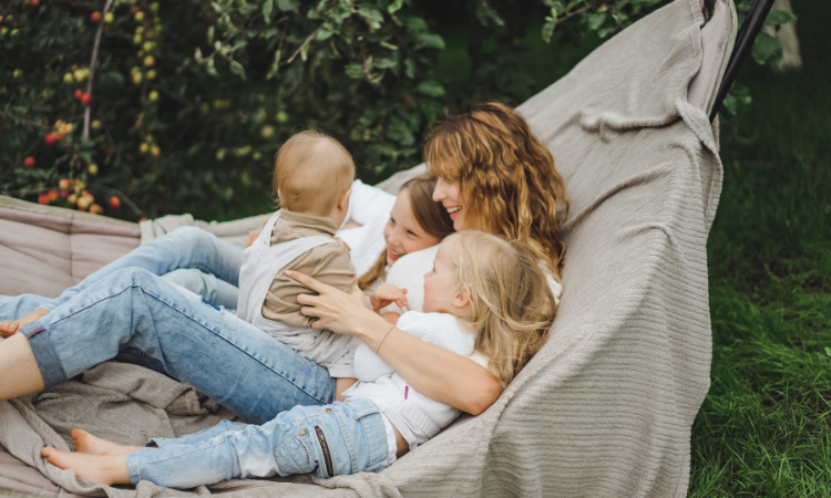 kobieta wypoczywająca z tr&oacute;jką dzieci na hamaku ogrodowym 