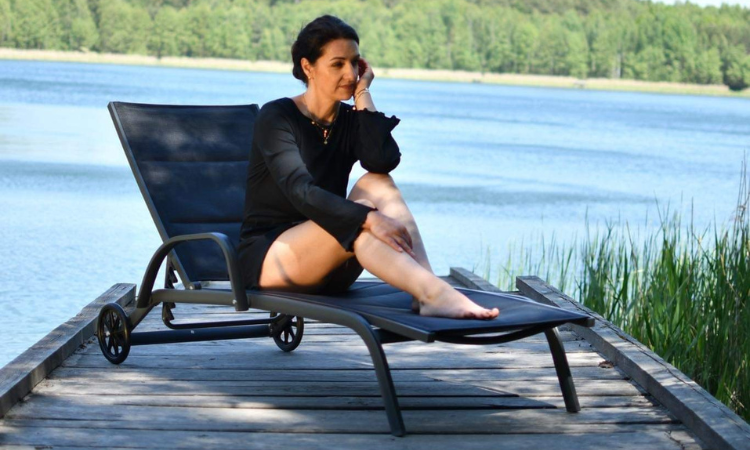 kobieta odpoczywajaca w czarnej letniej sukience na lezaku basenowym 