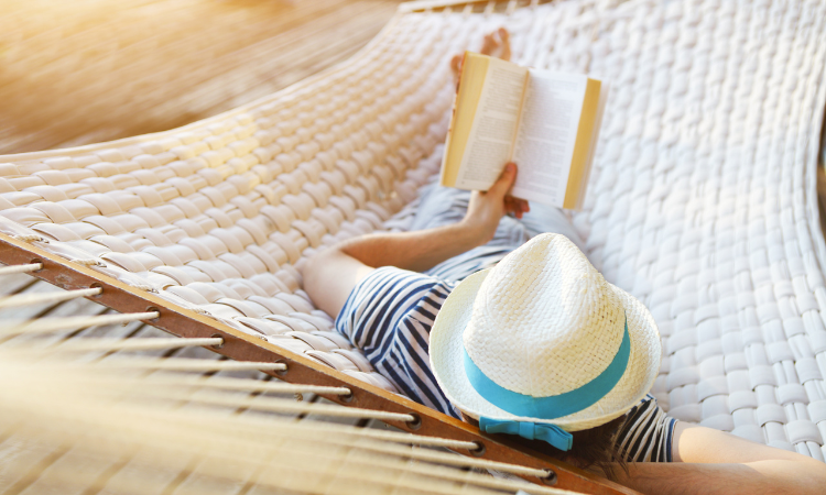 mężczyzna leżący na kamaku w kapeluszu i czytający książkę 