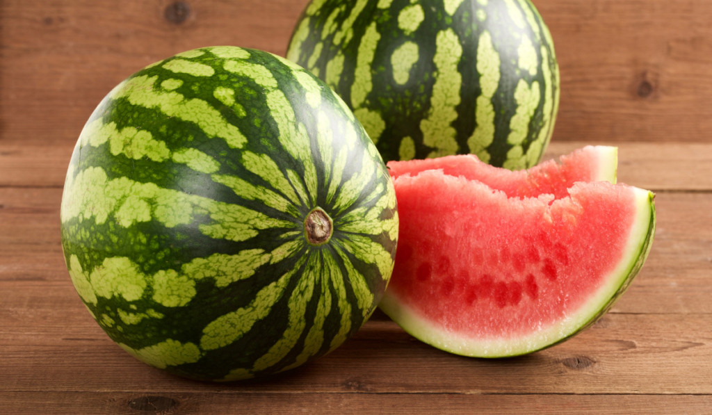 Dwa arbuzy i dwie pokrojone p&oacute;łksiężyce tego owoca