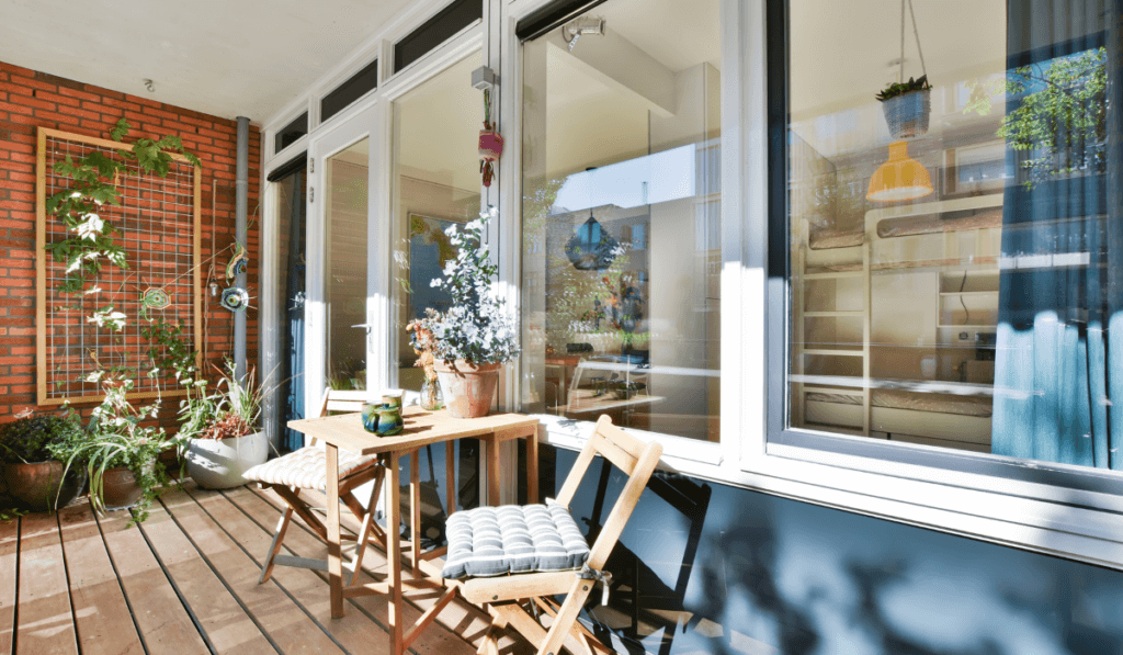 Ciepło urządzony balkon, z kwaitami meblami oraz innymi dodatkami, z drewnianymi meblami blkonowymi